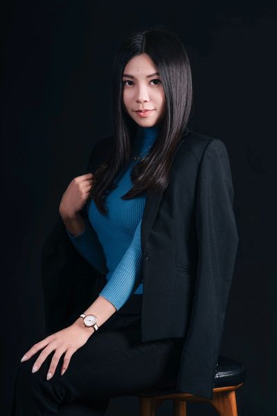 Confident woman in a blue top and black blazer poses against a dark background.
