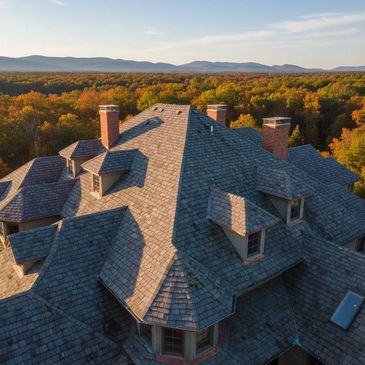 A large house roof with chimneys surrounded by autumn forest and mountains.