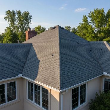 A house with a gray shingled hip roof and large windows surrounded by trees.