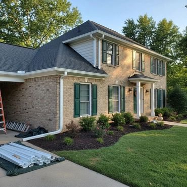 Two-story brick house with green shutters and landscaping under a clear sky.