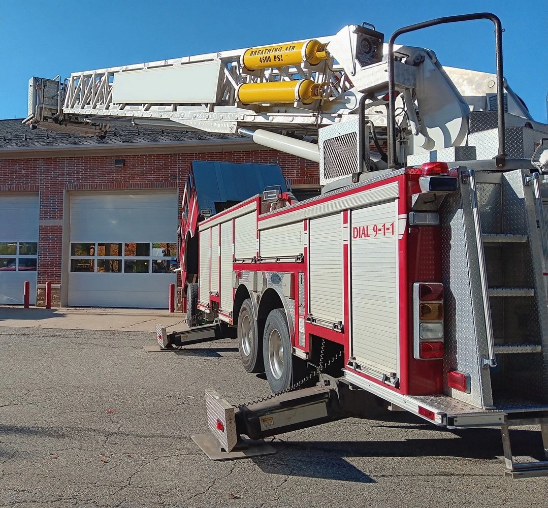 Fire truck with extended ladder parked outside a fire station on a clear day.