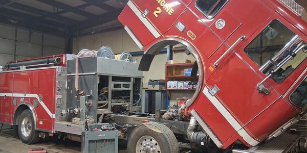 A red fire truck undergoing maintenance with its cab tilted forward.
