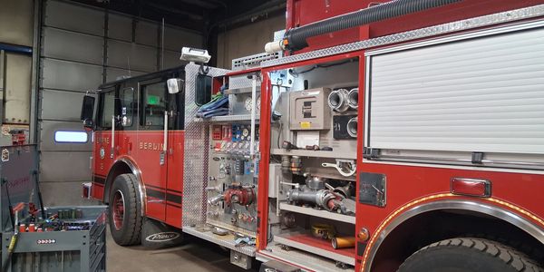 A red fire engine inside a garage with equipment compartments open and tools nearby.