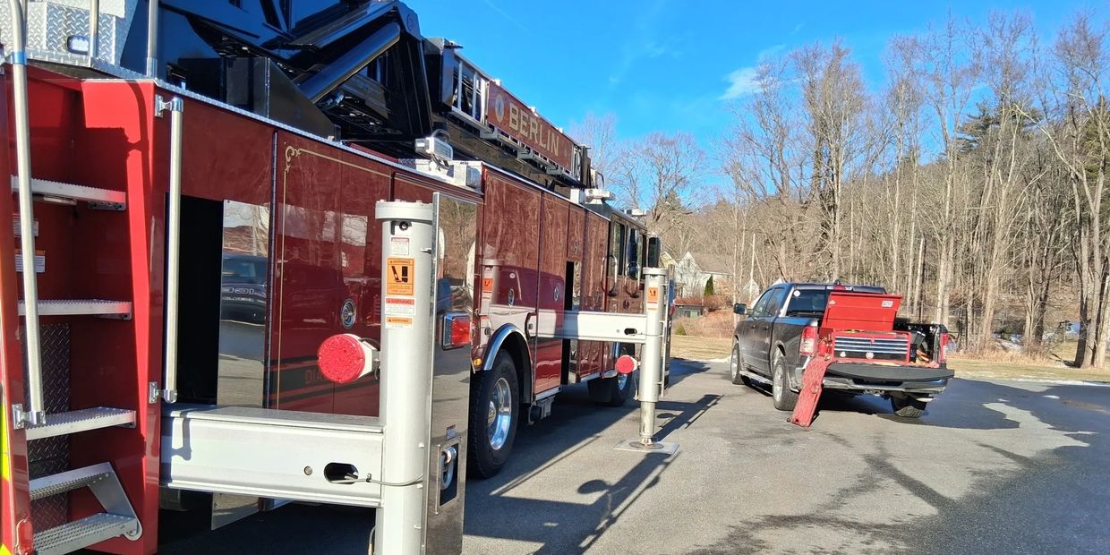 Fire truck with stabilizers deployed next to a pickup truck on a sunny day.