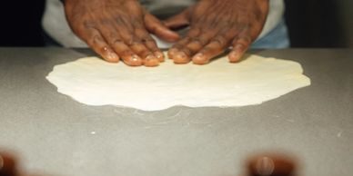 Person flattening dough on a surface.