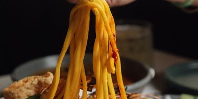 Hand lifting noodles from a plate.