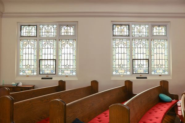 Wooden church pews with red cushions and stained glass windows.