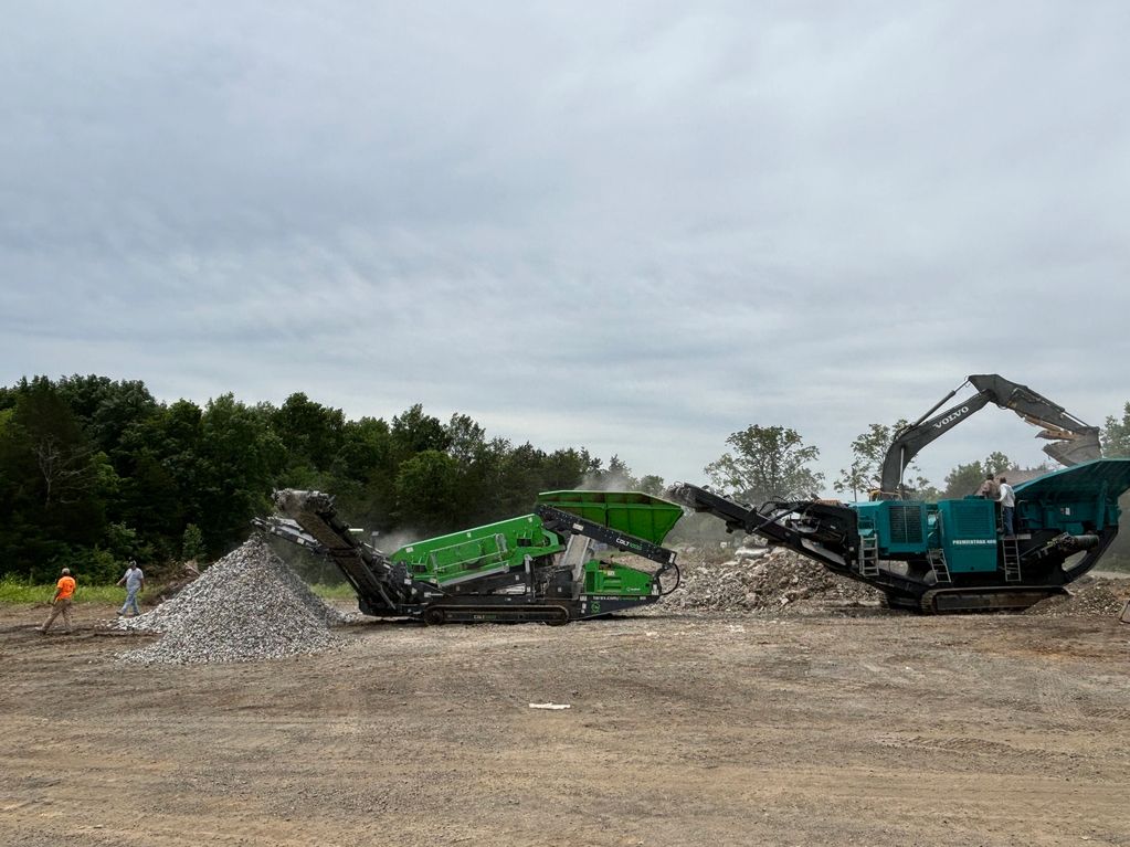 Heavy machinery processing rubble with two workers nearby on a cloudy day.