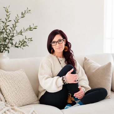 Woman in cozy sweater sitting on a beige couch with decorative pillows.