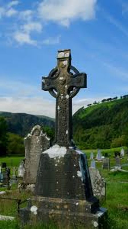 Old Celtic cross gravestone in a green cemetery under a blue sky.