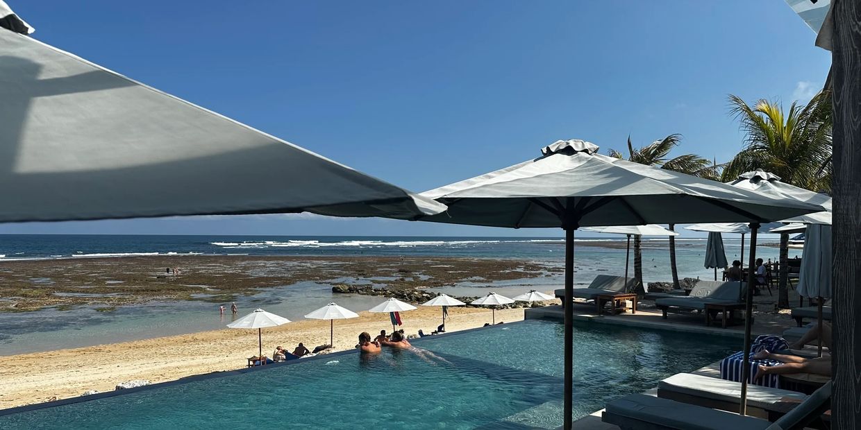Infinity pool overlooking a sandy beach and ocean under clear blue sky.