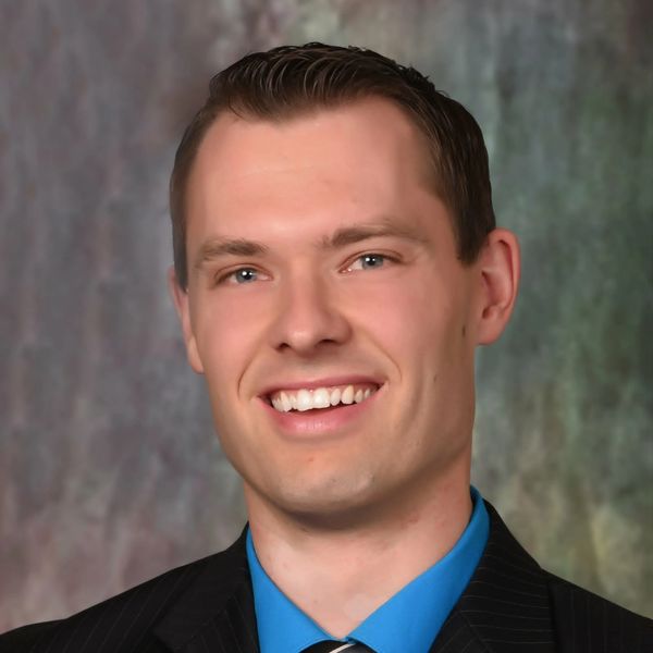 Smiling young man in a suit with a blue shirt and striped tie.