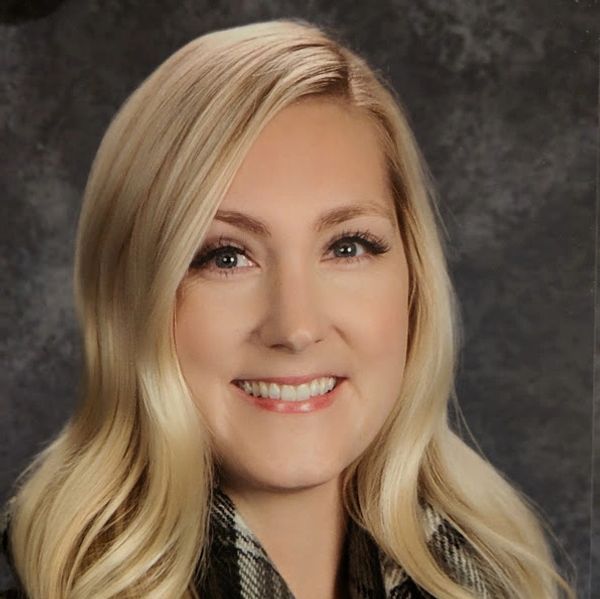 Portrait of a smiling blonde woman with wavy hair and a plaid scarf.