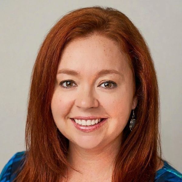 Smiling woman with red hair and light makeup.