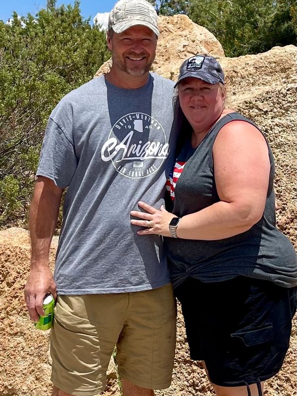 Smiling couple posing outdoors against rocky terrain on a sunny day.