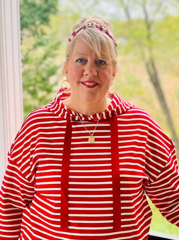 Woman in red and white striped hoodie smiling outdoors.