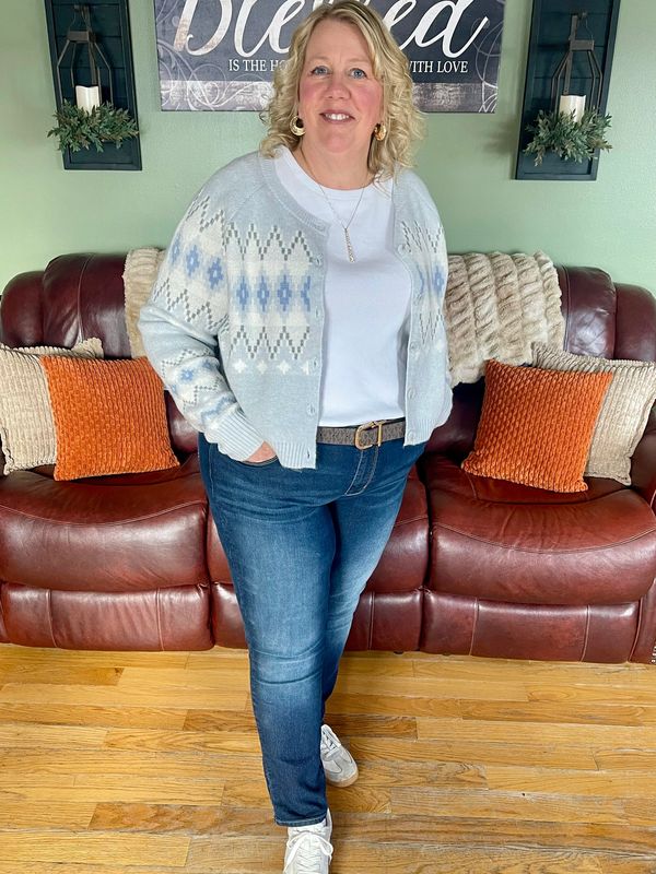 Woman standing in a cozy living room wearing a patterned cardigan and jeans.