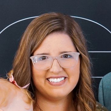 Smiling woman with glasses and wavy hair.