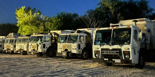 A row of white garbage trucks parked under the evening sky.