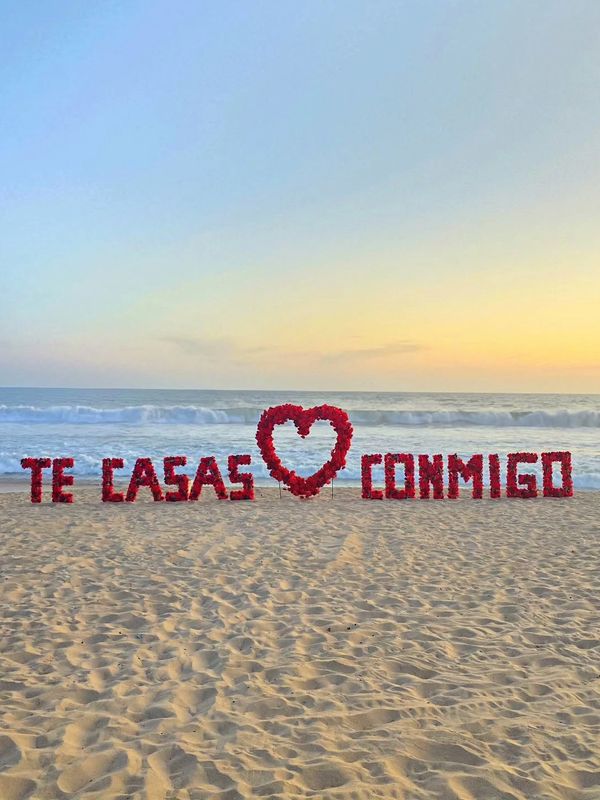 Marriage proposal on the beach at sunset with a heart and the words 'Te casas conmigo'.