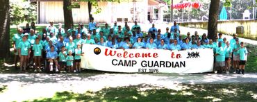 Group photo of Camp Guardian participants holding a welcome banner outdoors.