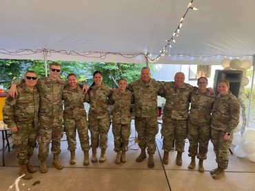 Group of soldiers in uniform standing together under a tent, smiling.