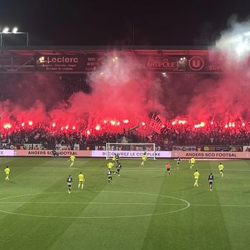 Soccer match with fans lighting red flares and waving flags in the stands at night.