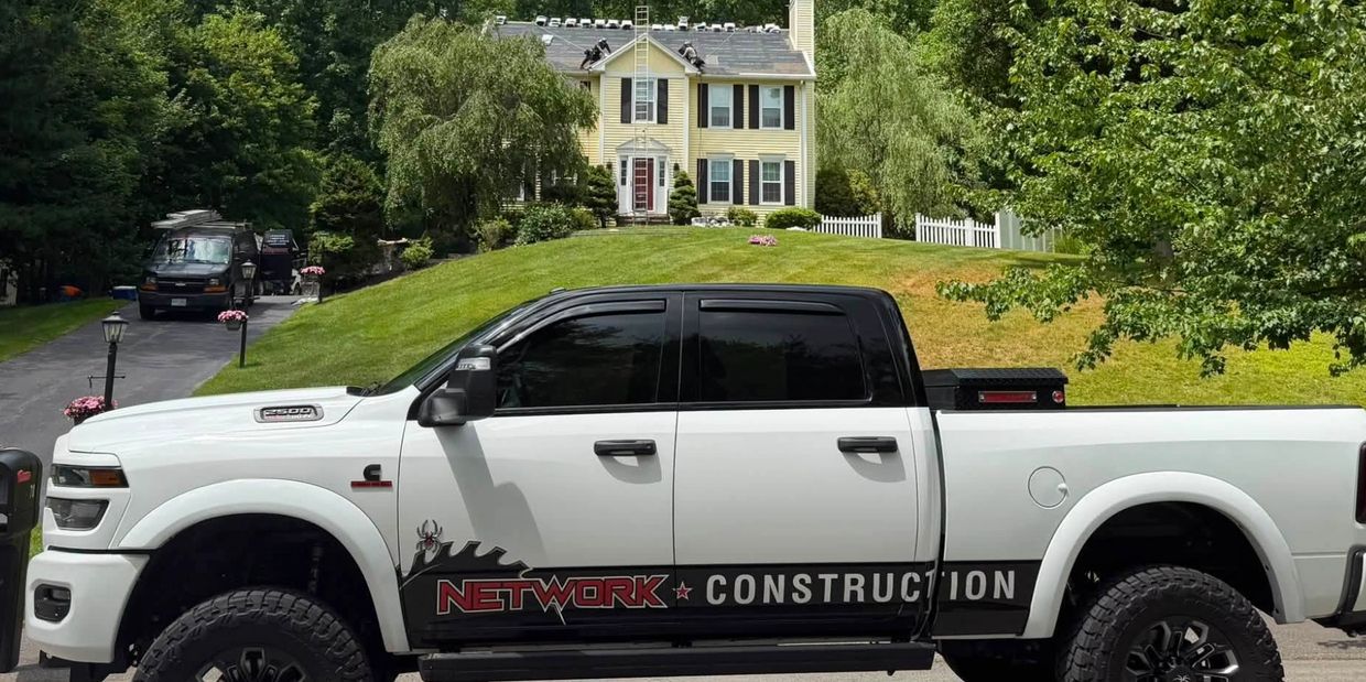 White Network Construction truck parked in front of a yellow house.