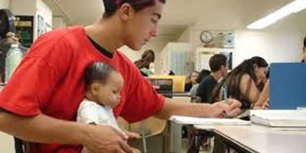 Young man studying while holding a baby in a classroom.