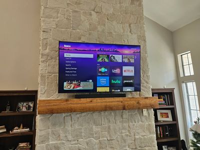 Flat-screen TV mounted above stone fireplace with wooden mantel.