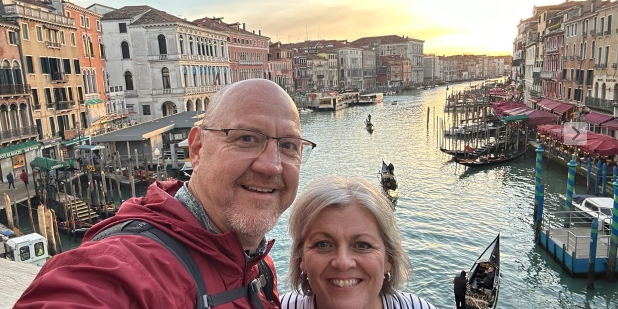 Couple taking a selfie on a bridge over a canal in Venice at sunset.