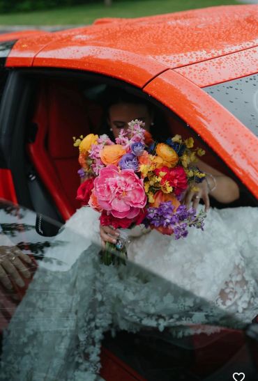 Bride holding colorful bouquet inside a red car.