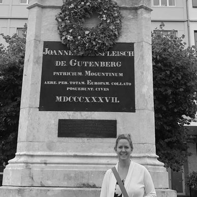 A woman standing in front of an old monument with a wreath on top.