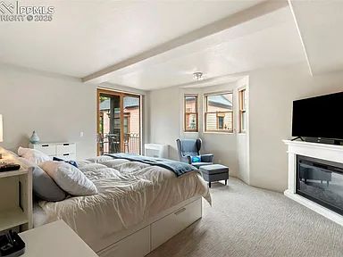 Bright bedroom with a cozy bed, armchair, and TV above a fireplace.