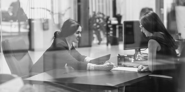 Two women engaged in a business discussion at an office desk.