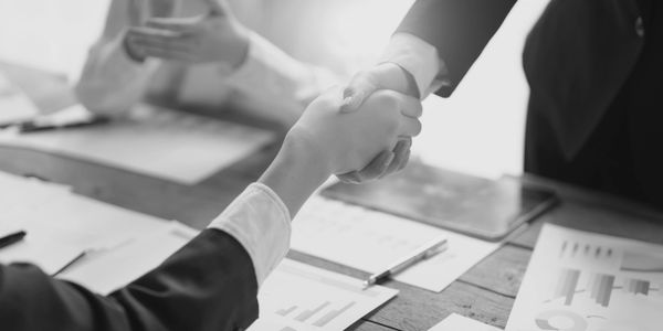 Two professionals shaking hands over a business table with documents.