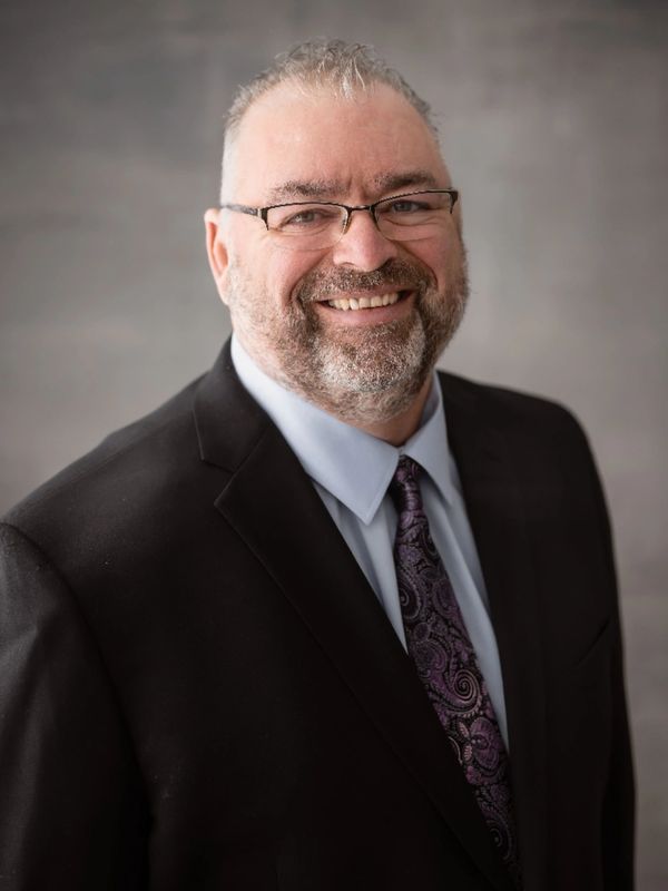 Smiling man in a suit and patterned tie, wearing glasses.