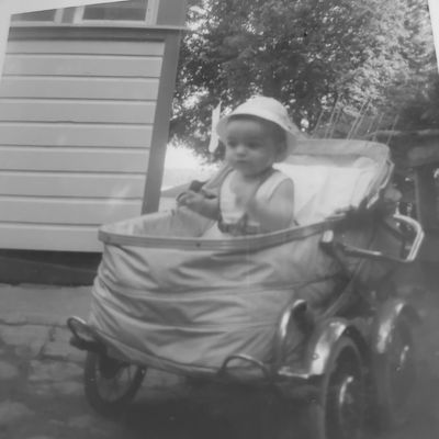 Baby sitting in an old-fashioned stroller outside a house.