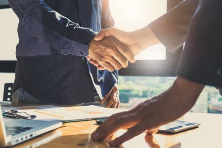 Two men shaking hands over business materials