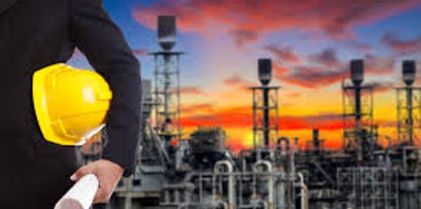 Engineer holding a yellow helmet and blueprint at industrial site during sunset.