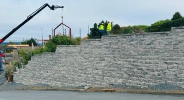 Construction workers building a large retaining wall with a crane.
