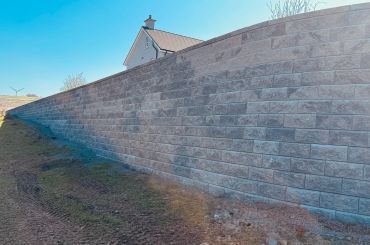 A long brick wall with a house roof visible behind it.