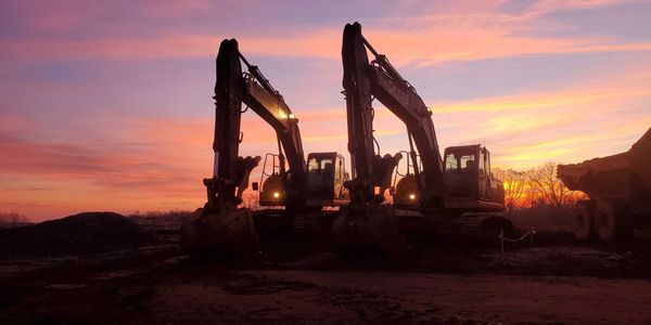 Two excavators with lights on at sunset on a construction site.