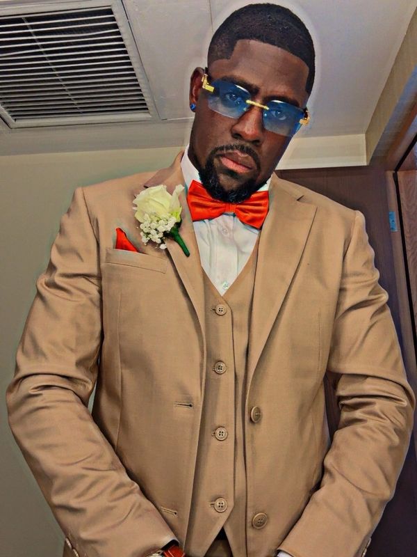 Man in beige suit with red bow tie and blue sunglasses.
