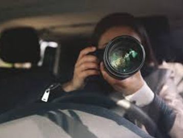 Person inside car holding a large camera lens, taking a photo.