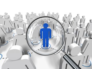 Magnifying glass highlighting a blue figure among gray figures, symbolizing focus or selection.