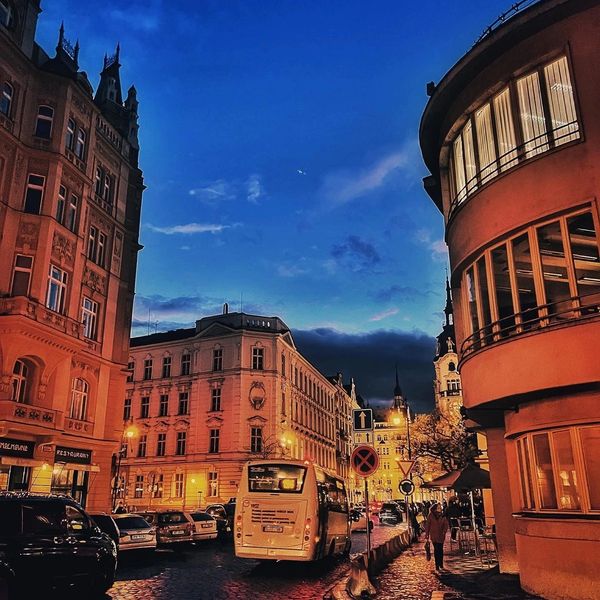 Evening street scene with historic buildings and glowing streetlights under a deep blue sky.