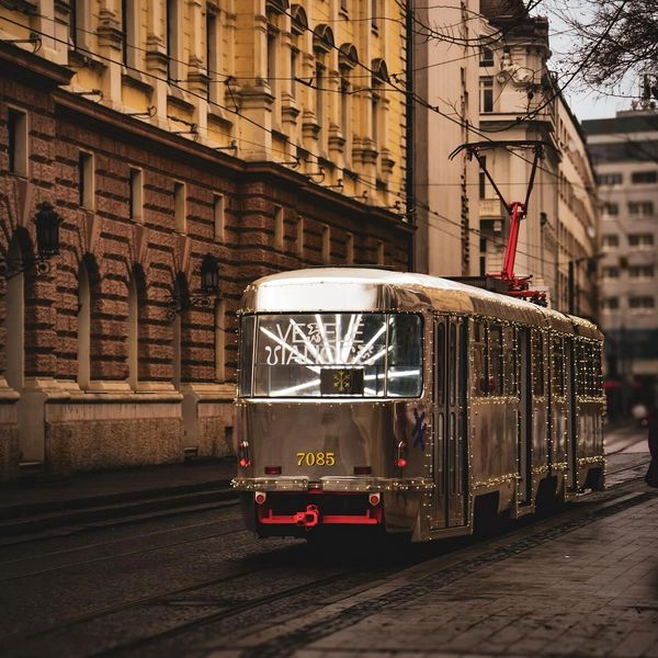 A vintage tram decorated with lights travels through a historic city street at dusk.
