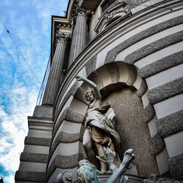 Statue in an ornate alcove beneath classical columns against a blue sky.