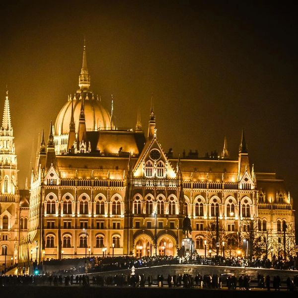 Illuminated grand historic building at night with crowd gathered.